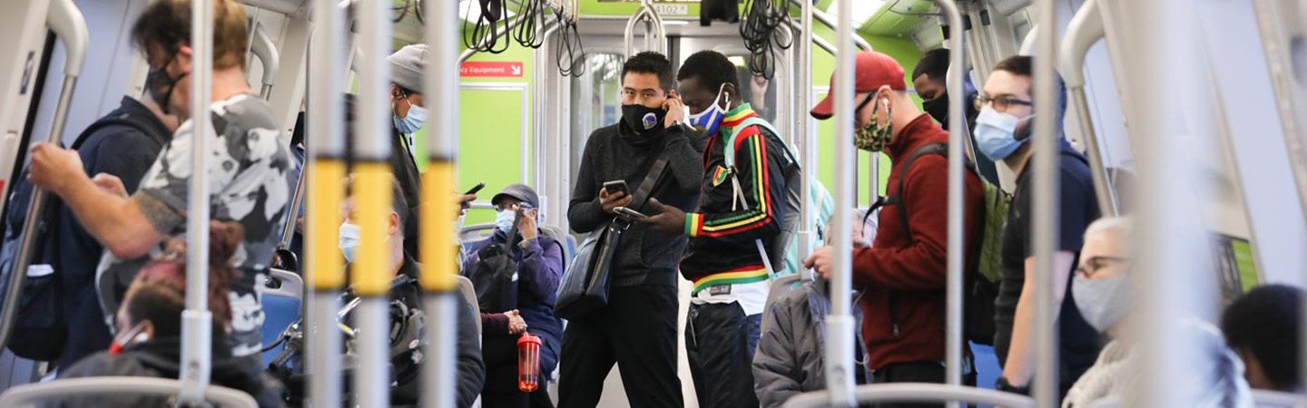 A group of masked passengers stands inside a busy BART train.