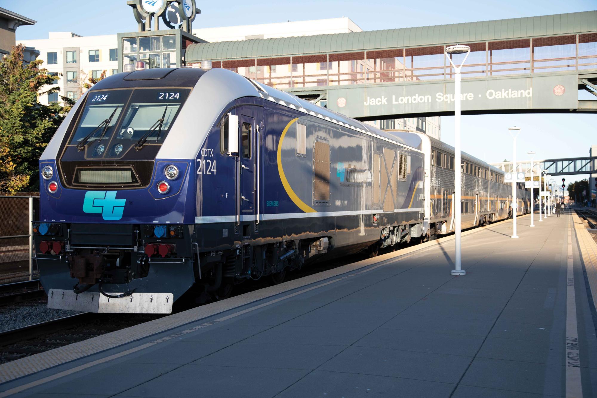 A Capitol Corridor train sits at the Jack London Square station in Oakland with a large shadow encompassing half the platform.